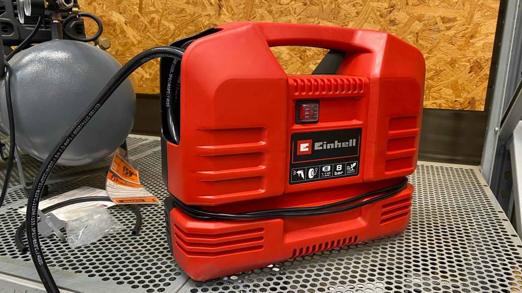 Tragbarer Kompressor im Test: ein rotes Gerät von Einhell steht auf einem Lochregal.
