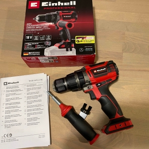 Das Bild zeigt den Einhell Professional Akku-Schlagbohrschrauber TP-CD 18/70 Li BL im unbenutzten Zustand neben der Originalverpackung. Das Zubehör wie Zusatzgriff und Anleitung sind ebenfalls zu sehen.