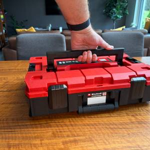 Eine Hand hält den Einhell-Werkzeugkoffer am großen Griff auf der Oberseite fest