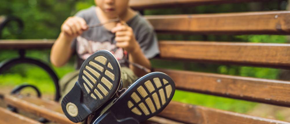Kinder-Einlegesohlen-Test: Ein kleiner Junge sitzt mit ausgestreckten Beinen auf einer Gartenbank aus Holz, sodass man die Sohle seiner Schuhe erkennen kann.