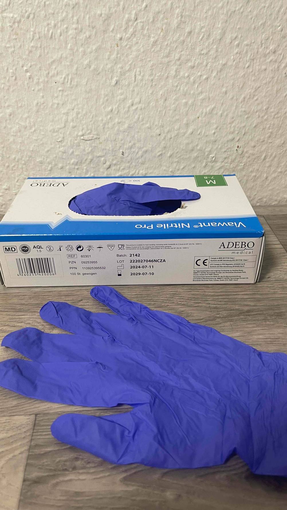 Der violette Einmalhandschuh im Test liegt vor dem Spender-Karton, welcher auf einer Holzfläche steht.