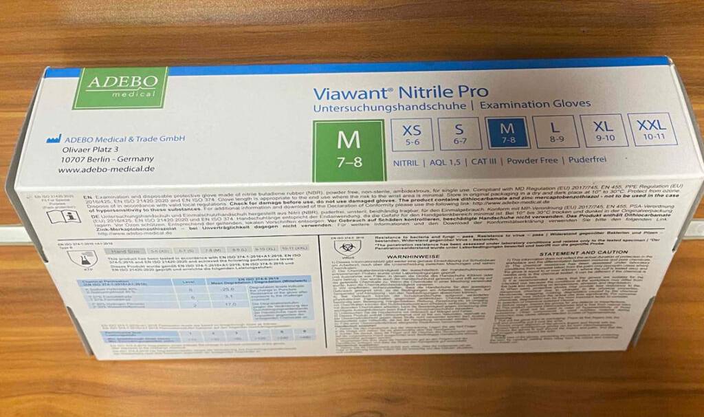 Nahaufnahme der Produktinformationen auf einem weißen Spender-Karton, der auf einer Holzfläche steht und die Einmalhandschuhe im Test enthält.