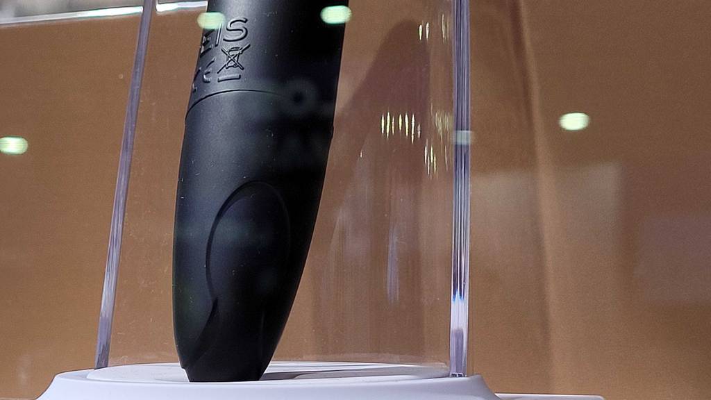 Squirting-Dildo im Test: Nahaufnahme eines schwarzen Dildos der Marke Eis. Er befindet sich in einem Plexiglas-Ständer vor braunem Hintergrund.