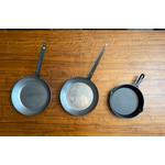 Drei Eisenpfannen liegen nebeneinander auf einem Tisch