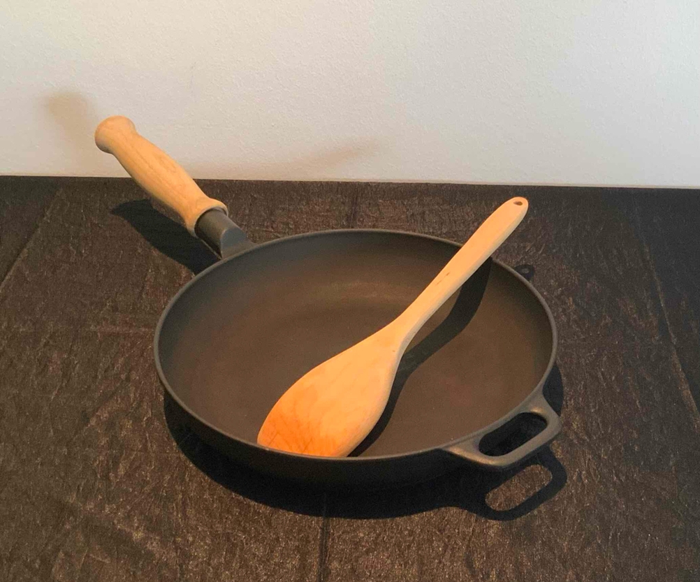 Im Test: Eine Eisenpfanne von schräg oben mit einem Kochlöffel auf einer dunklen Fläche.