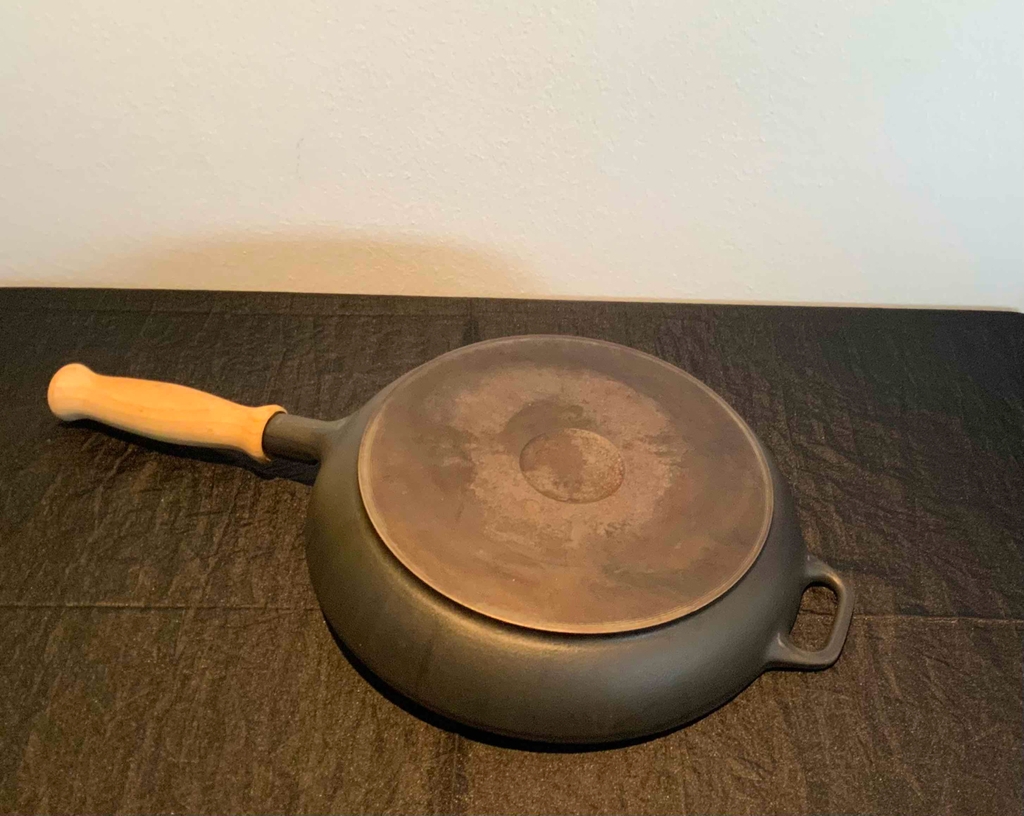 Eine getestete Eisenpfanne liegt mit dem Boden nach oben auf einer dunklen Fläche.