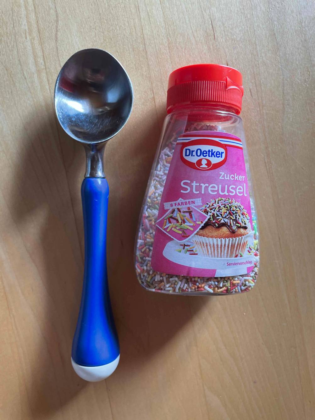Ein getesteter Eisportionierer liegt neben einer Packung mit Streuseln auf einer Holzfläche.