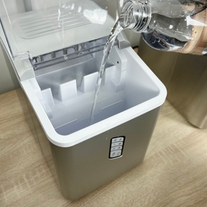 Eine Hand gießt Wasser aus einer Flasche in den geöffneten Tank der Conopu ICM1227. Der Deckel ist geöffnet.