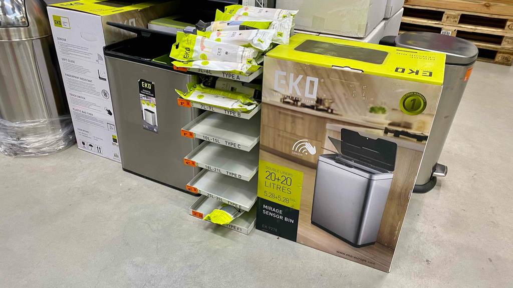 Ein silberfarbener Mülleimer mit Sensor im Test steht in einem Verkaufsbereich in der Nähe seiner EKO-Originalverpackung.