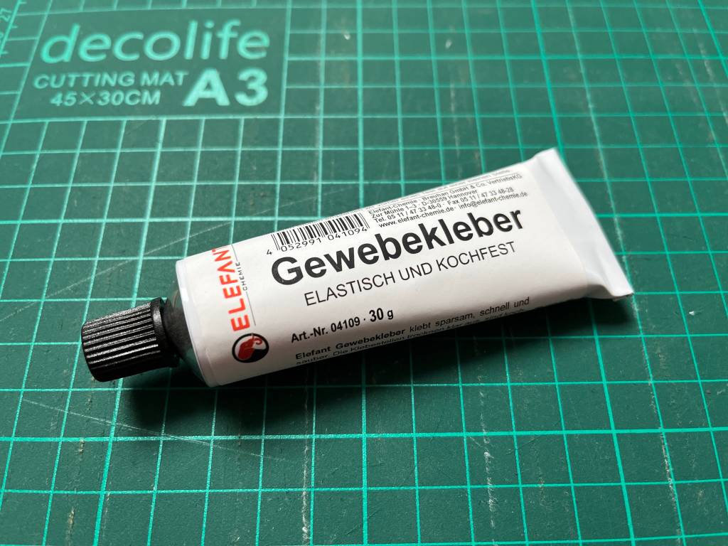 Stoffkleber in weißer Tube auf einer Zuschnittplatte für Stoff