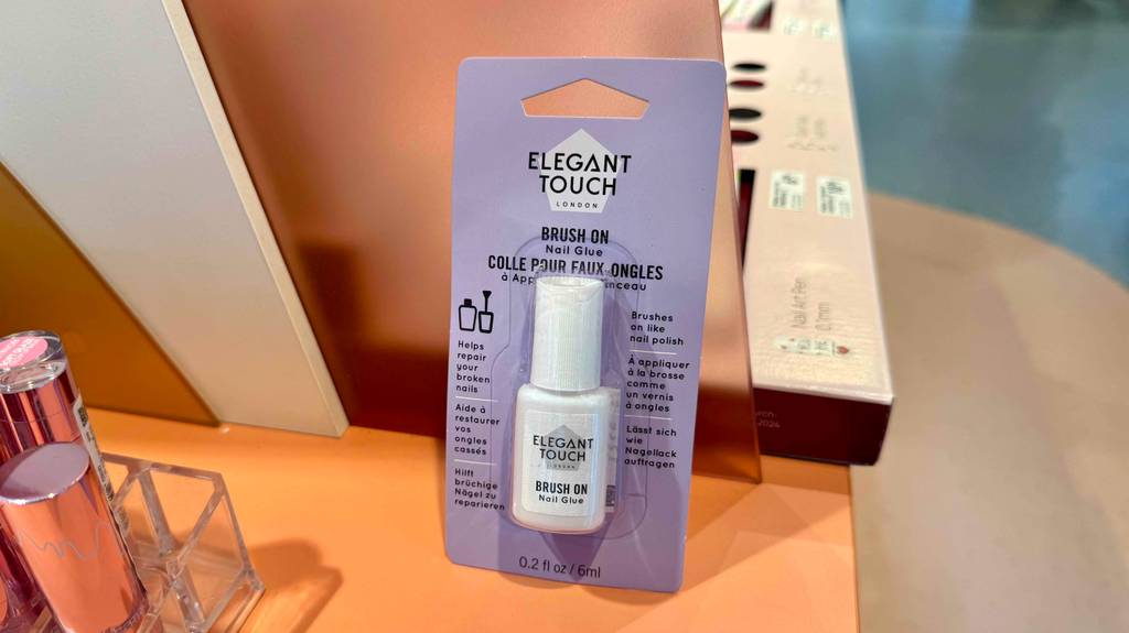 Eine Flasche Nagelkleber im Test befindet sich eingeschweißt in seiner Verpackung im Kosmetikbereich eines Drogeriemarktes.