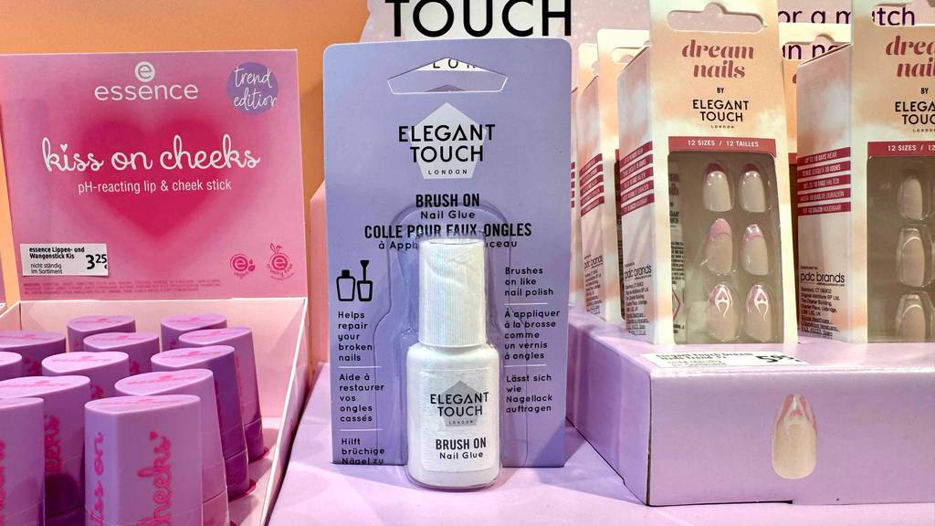 Getestet: Nagelkleber im Test befindet sich eingeschweißt in seiner Verpackung in einer 6-ml-Flasche im Kosmetikbereich neben falschen Fingernägel-Packungen.