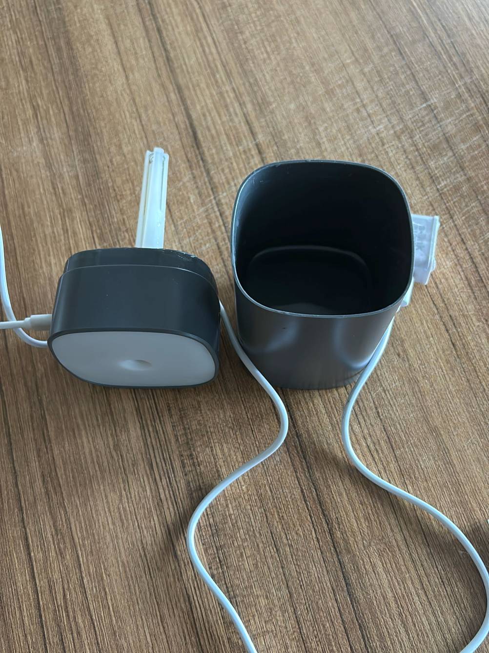 Elektrische Duftlampe getesttet: Ein geöffnetes Gerät mit Kabel, Behälter neben dem Deckel auf einer Holzfläche.