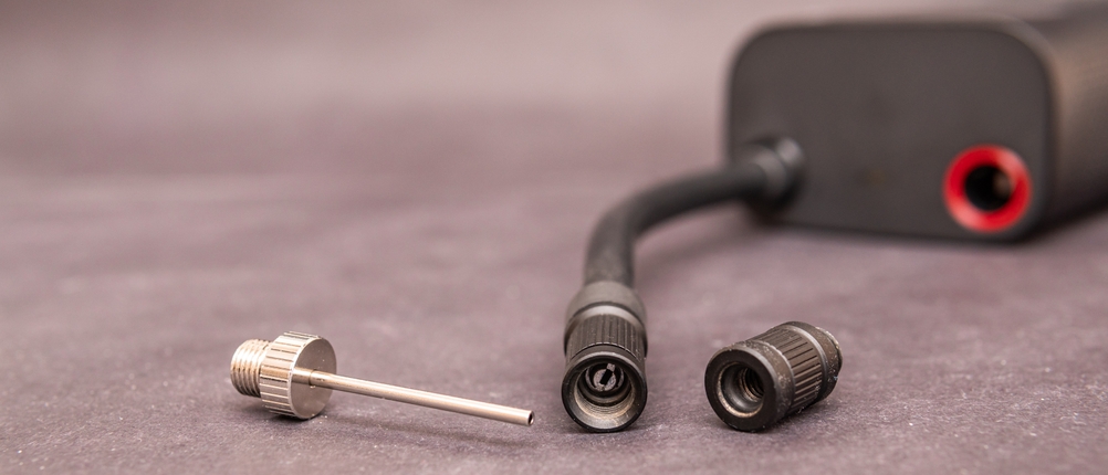 Drei Adapteraufsätze liegen neben dem Luftschlauch einer elektrischen Fahrradpumpe auf einer grauen Oberfläche.