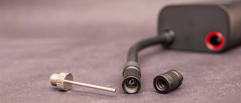 Drei Adapteraufsätze liegen neben dem Luftschlauch einer elektrischen Fahrradpumpe auf einer grauen Oberfläche.