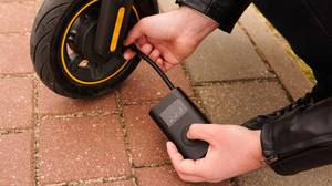Ein E-Scooter-Reifen wird mit einer elektrischen Fahrradpumpe auf einem Pflasterweg aufgepumpt.