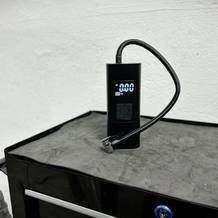 Die Neakhmer Luftkompressor Fahrradpumpe steht mit angeschlossenem Luftschlauch auf einer Werkbank. Das Display zeigt den Betriebsstatus an.