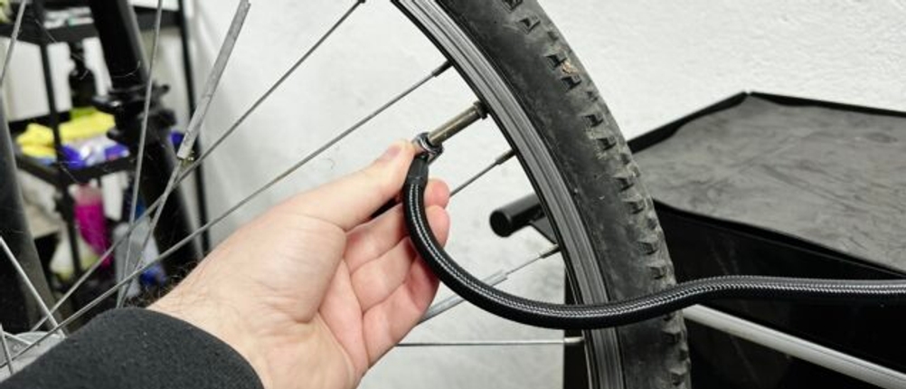 Eine Hand hält den Luftschlauch der Neakhmer Luftkompressor Pumpe an ein Fahrradventil. Der Anschluss erfordert einen Adapter für Dunlop-Ventile.