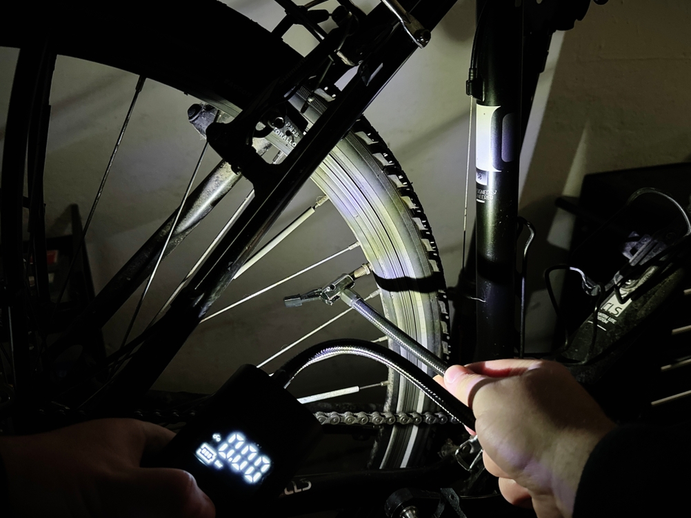 Die Neakhmer-Luftkompressor-Fahrradpumpe leuchtet mit ihrer integrierten Taschenlampe auf ein Fahrradventil. Das Display ist beleuchtet.