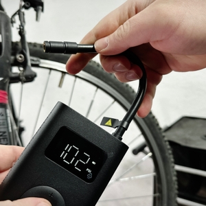 Eine Hand zieht den Luftschlauch aus der Xiaomi-Fahrradpumpe, um das Gerät einzuschalten. Das Display zeigt den aktuellen Druck an.