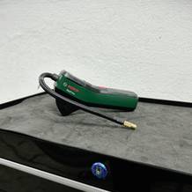 Die Bosch Easypump 603947000 liegt auf einer Werkbank, mit aufgerolltem Luftschlauch und Ventilaufsatz. Das kompakte Design ist gut erkennbar.