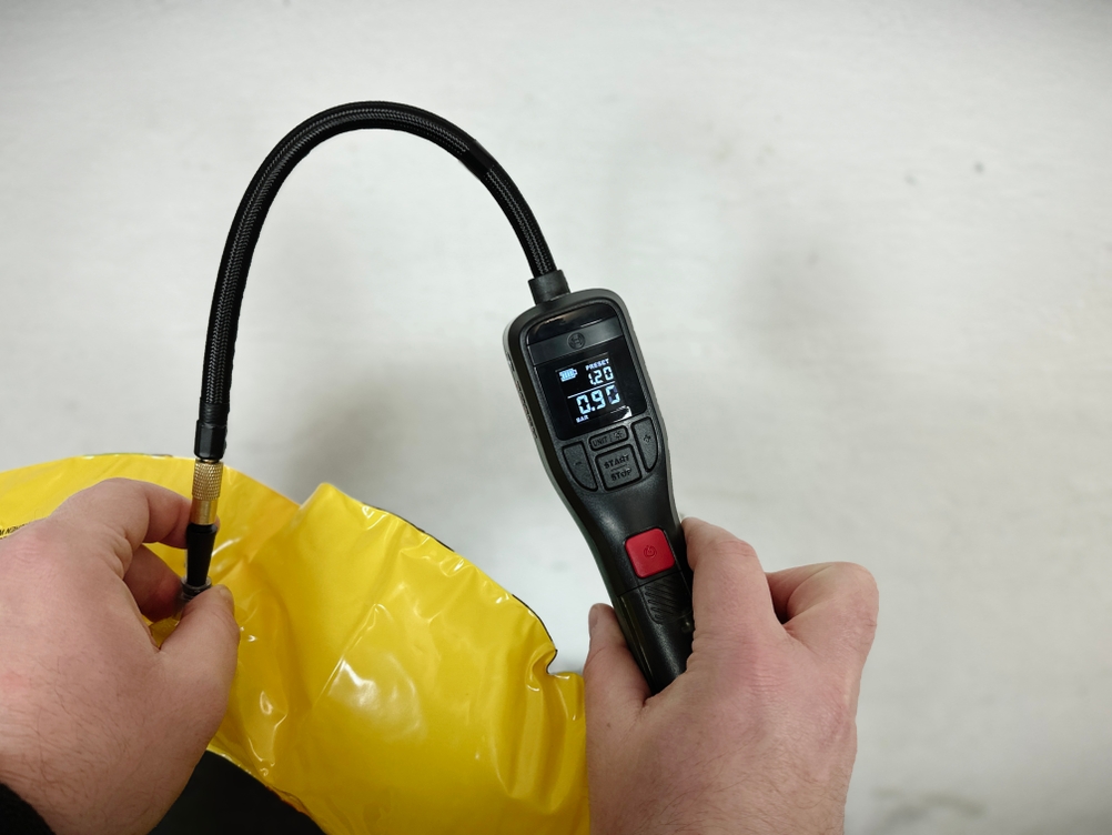 Eine Hand hält einen gelben, nicht vollständig aufgepumpten Schwimmreifen. Die Bosch Easypump ist angeschlossen und zeigt den aktuellen Luftdruck an.