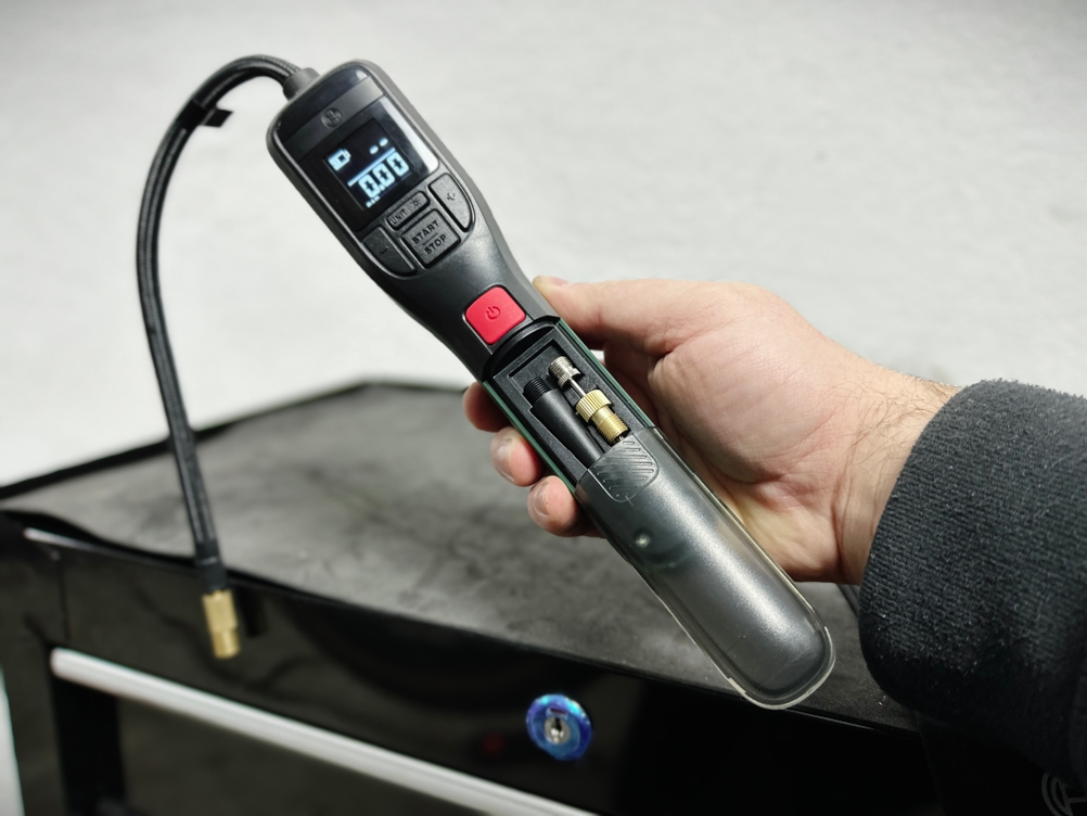 Eine Hand hält die Bosch Easypump mit geöffnetem Zubehörfach, in dem Ventiladapter sicher verstaut sind.