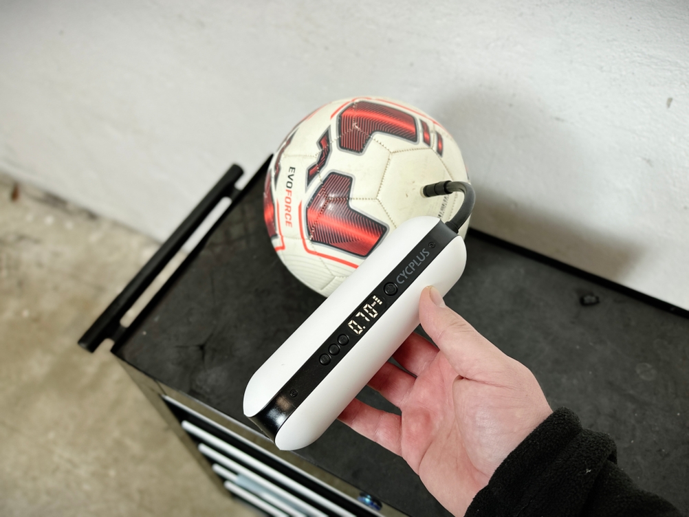 Eine Cycplus elektrische Luftpumpe pumpt einen Fußball auf. Der aktuelle Druck wird auf dem Display angezeigt.