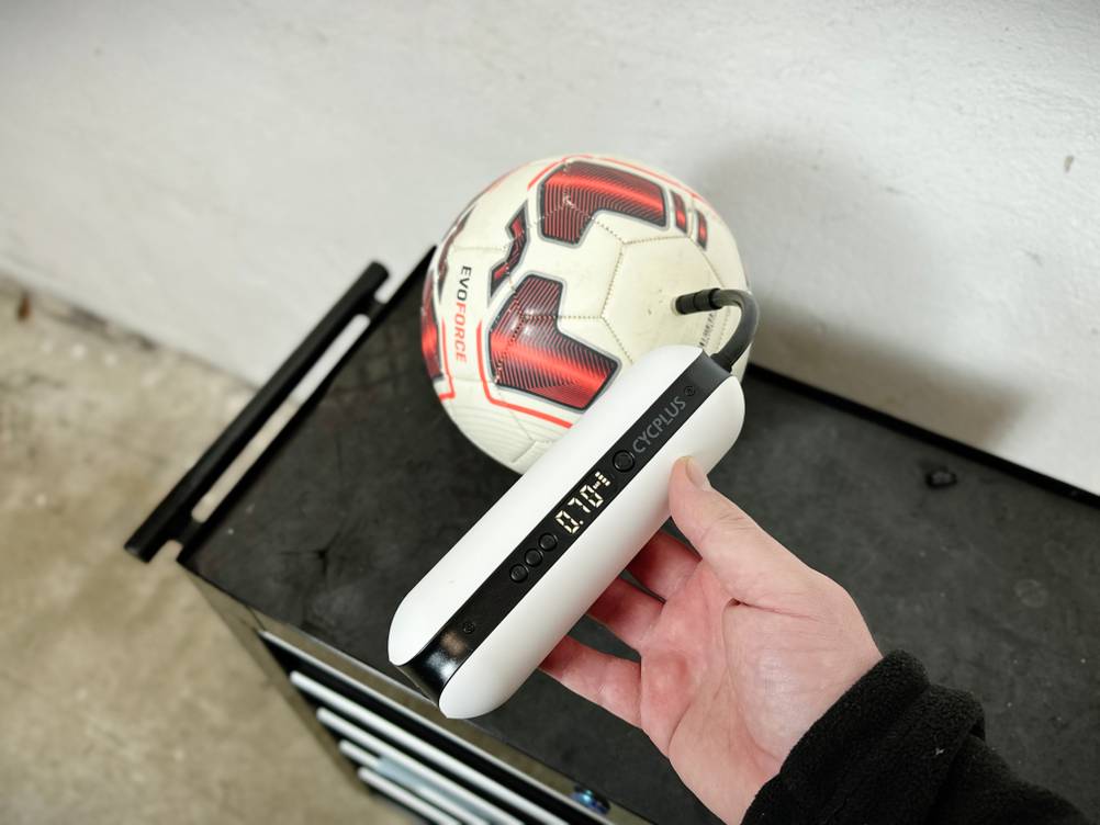 Eine Cycplus elektrische Luftpumpe pumpt einen Fußball auf. Der aktuelle Druck wird auf dem Display angezeigt.