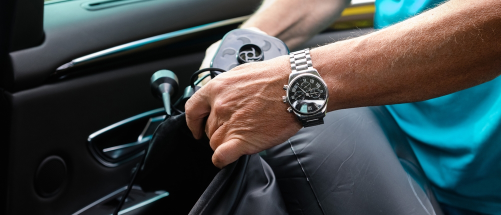 Eine Person nutzt im Auto eine elektrische Luftpumpe, um eine Luftmatratze aufzublasen. Das Gerät ist an das Ventil der Matratze angeschlossen.