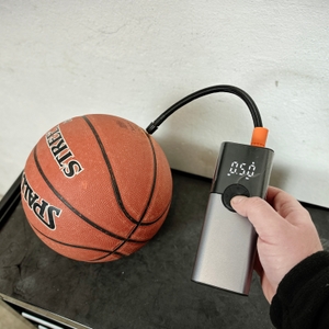 Eine Hand hält die Zoruman CZK-3686, während sie einen Basketball aufpumpt. Das Display zeigt den aktuellen Luftdruck und die voreingestellte Druckstufe an.