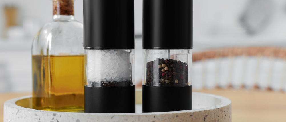 Elektrische Pfeffermühle im Test: Elektrische Salz- und Pfeffermühlen mit schwarzen Elementen stehen zusammen mit einer Flasche Öl auf einem Tablett.