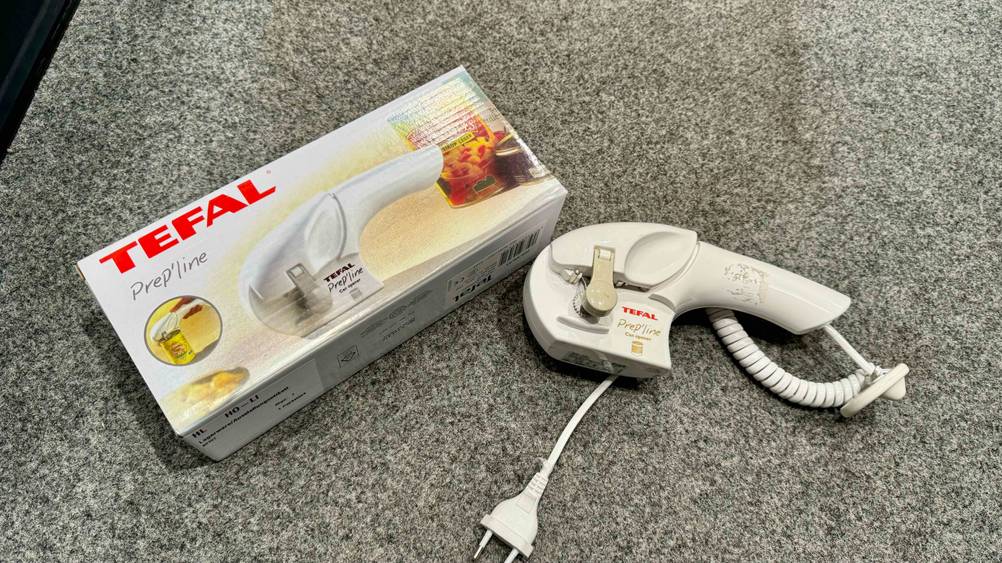 Auf einem grauen Boden liegt der getestete elektrische Dosenöffner neben seiner Originalverpackung.