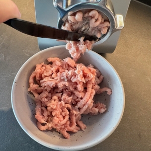 Fleischreste werden mit einem Messer von der Öffnung des Elektrischen Fleischwolf von Nictemaw entfernt