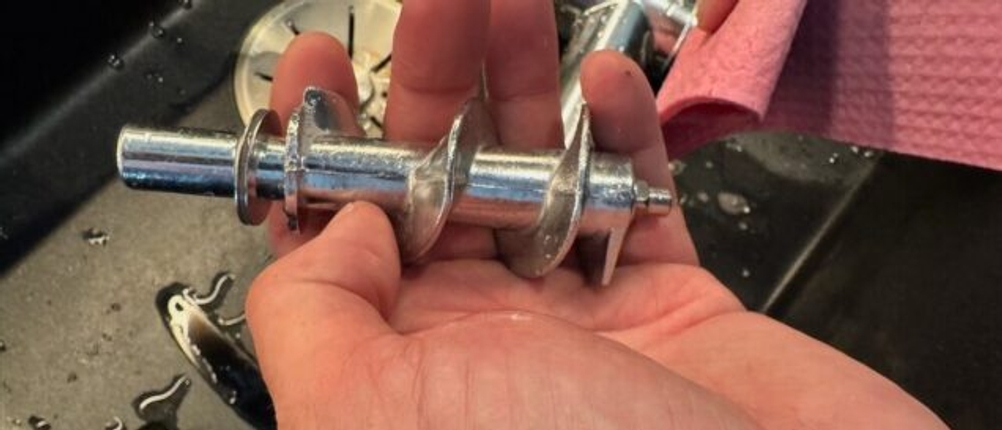 Eine Hand hält den Zerkleinerer des Elektrischen Fleischwolf von Nictemaw nach der Reinigung fest