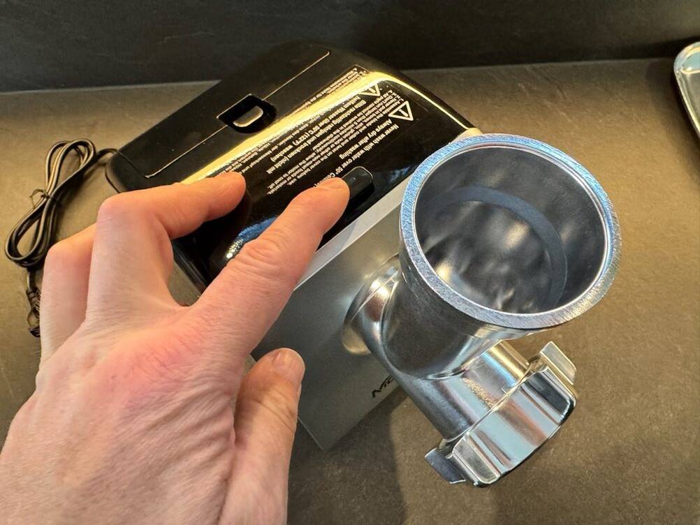 Eine Hand drückt einen Knopf auf dem Elektrischen Fleischwolf von Nictemaw