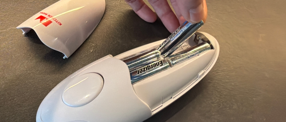 Eine Hand legt eine Batterie in den elektrischen Kitchen-Mama-Auto-Dosenöffner
