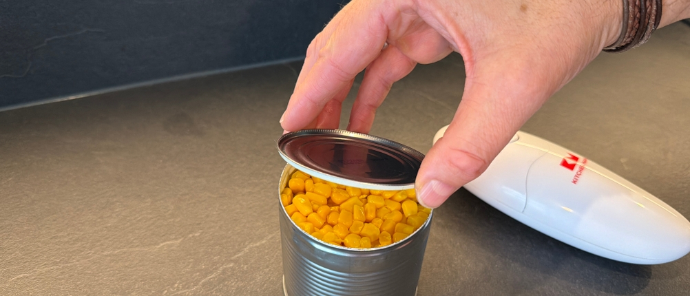 Eine Hand nimmt den Deckel von einer mit dem elektrischen Kitchen-Mama-Auto-Dosenöffner geöffneten Dose