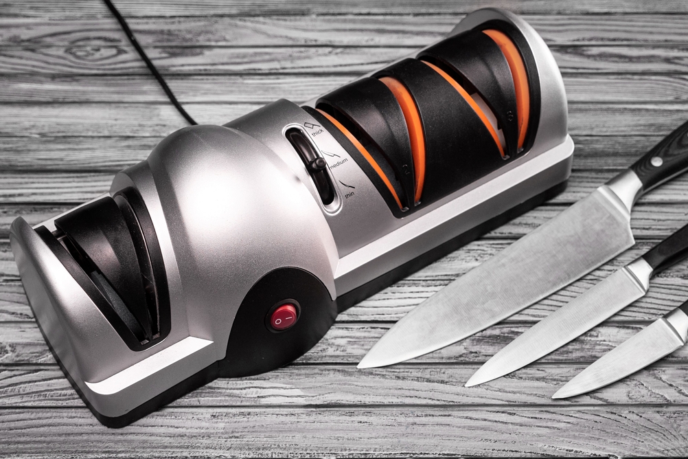 Ein elektrischer Messerschärfer steht eingesteckt neben drei Messern.