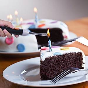 Mit einem Elektro-Feuerzeug wird die Kerze auf einem Kuchenstück angezündet.