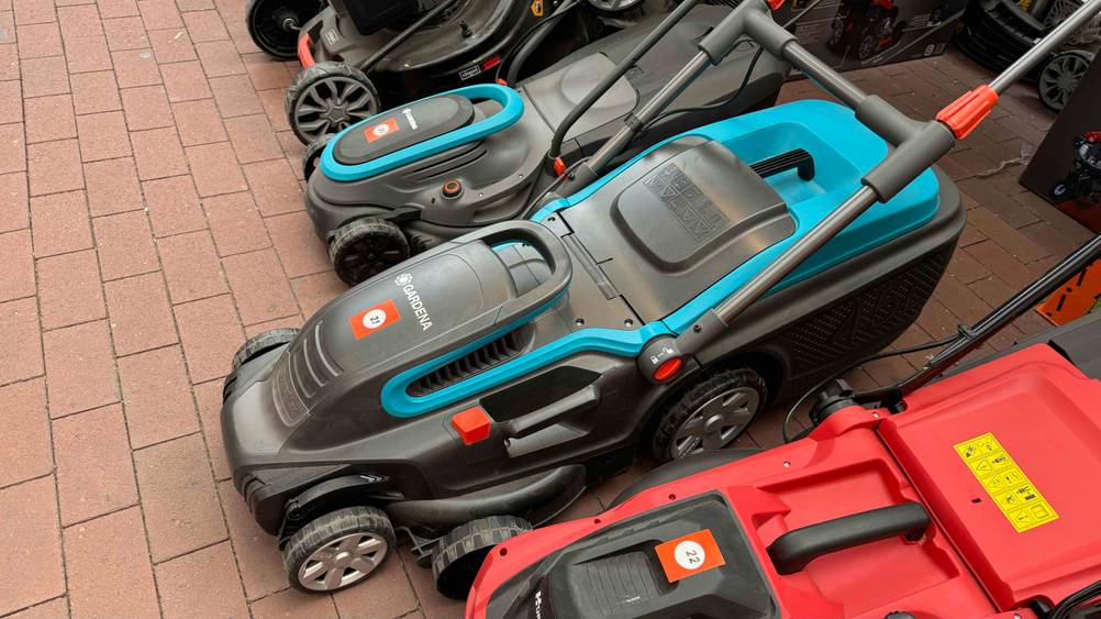 Ein getesteter Elektro-Rasenmäher mit Mulchfunktion neben anderen Geräten von schräg oben.