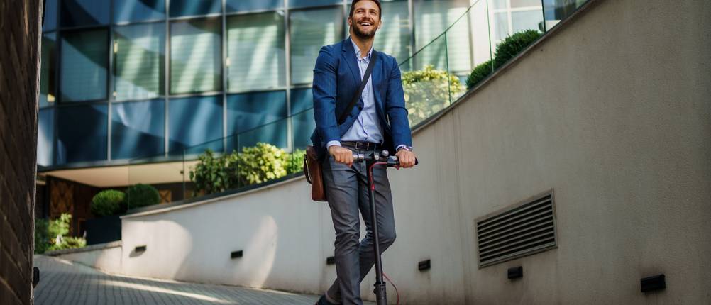 Elektro-Scooter-Test: Geschäftsmann im Anzug fährt auf einem Elektroroller zu einem Geschäftstreffen