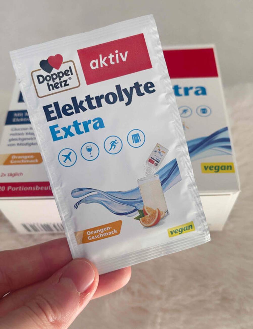 Eine Hand hält ein Päckchen des getesteten Elektrolyt-Pulvers vor die Packung.