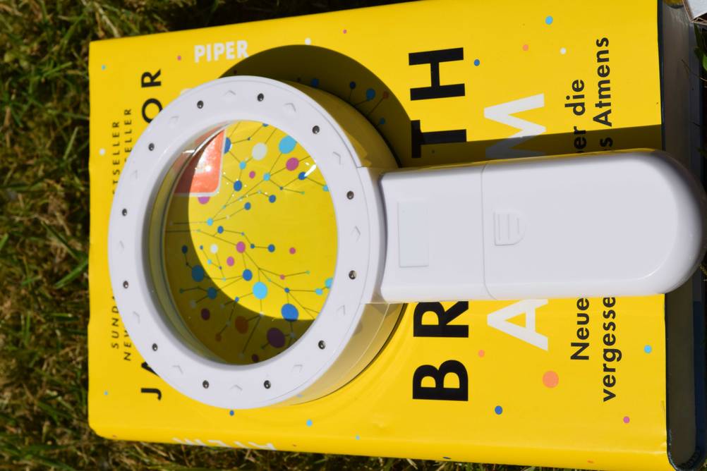 Eine getestete elektronische Lupe liegt mit den LED-Lichtern nach oben auf einem gelben Buch.