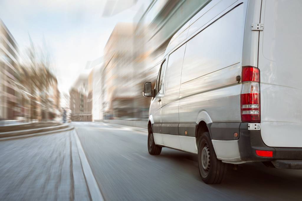 Ein weißer Transporter fährt durch die Stadt, während die Häuser verschwommen dargestellt werden.