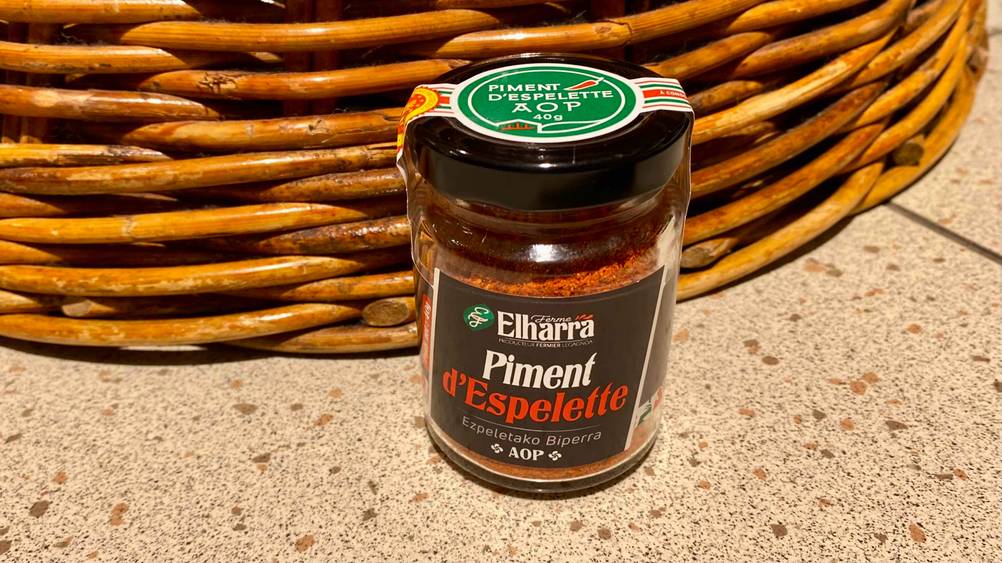 Piment d'Espelette getestet: Ein Glas von vorne vor einem Korb auf einer Fließenoberfläche.