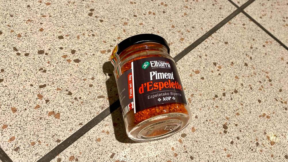 Ein Glas des getesteten Piment d'Espelette von unten mit Nahaufnahme auf den Boden auf einer Fließenfläche liegend.