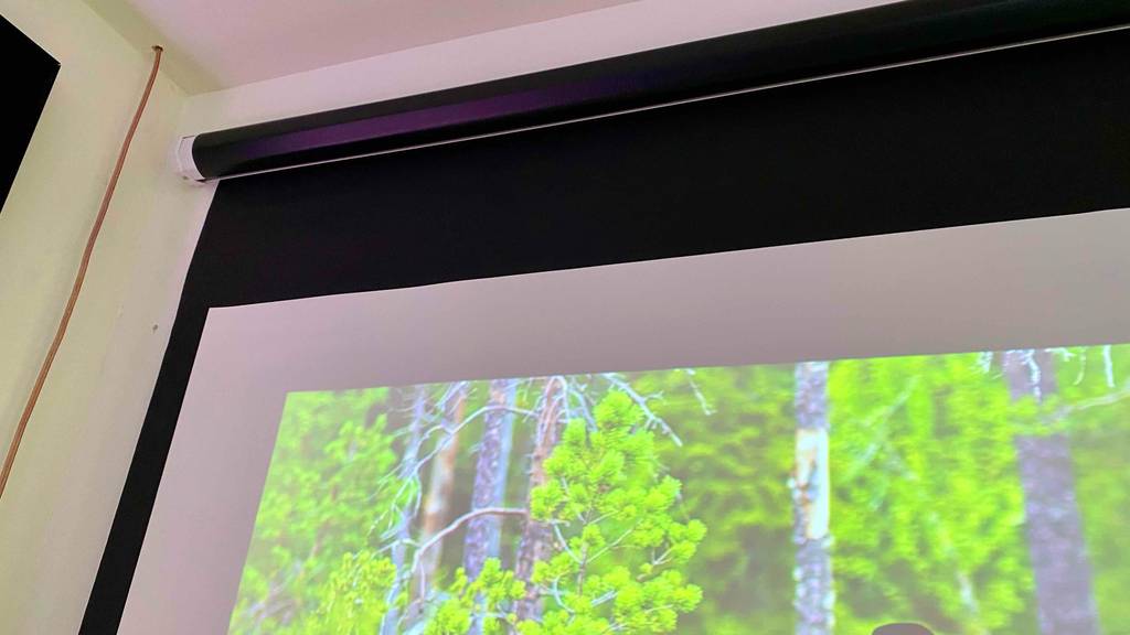 Detailansicht einer ausziehbaren schwarzen Rahmenleinwand im Test, die an einer weißen Wand montiert ist.