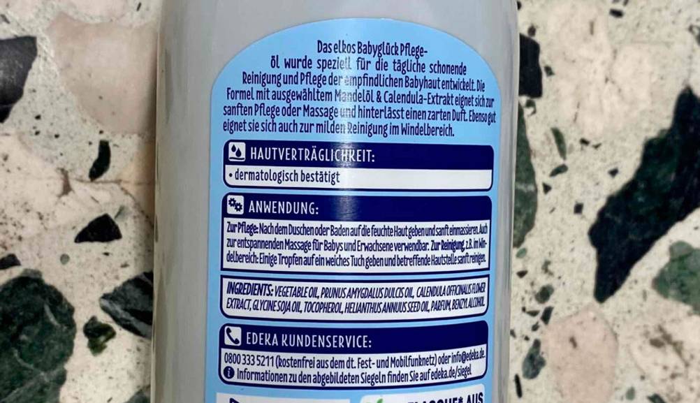Nahaufnahme der rückwärtigen Produktbeschreibung auf einer weißen Kunststoffflasche mit Babyöl im Test.