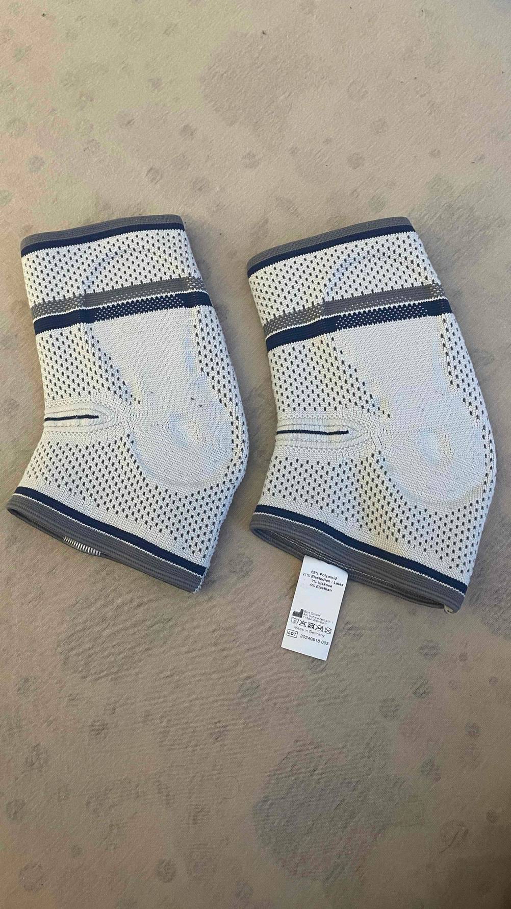 Im Test: Zwei Ellenbogenbandagen liegen nebeneinander auf einer hellen Fläche.